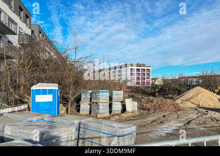 Un cantiere con pali di sabbia e ghiaia e pallet di pietre per pavimentazione avvolti in pellicola di plastica. Una recinzione metallica è visibile in primo piano, wh Foto Stock