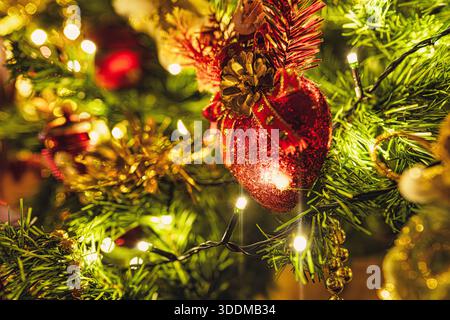 Rami dell'albero di Natale decorati con un ornamento rosso scintillante a forma di cuore, un cono di pino, un nastro, luci a corda illuminate e tinsel dorato, creat Foto Stock