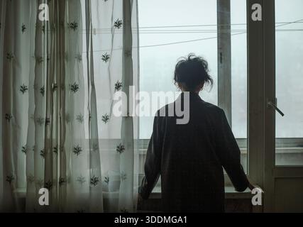 Una donna anziana sta alla finestra in inverno Foto Stock