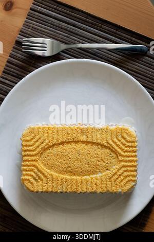 Una foto a 90 gradi della tradizionale insalata Ucraina Mimosa su un piatto bianco in cima a un tavolo di legno, che mostra la sua colorata presentazione a strati Foto Stock