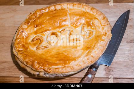 Torta di Capodanno fatta in casa con 2026 di pasta sfoglia sul tavolo della sala da pranzo con coltello giapponese Foto Stock