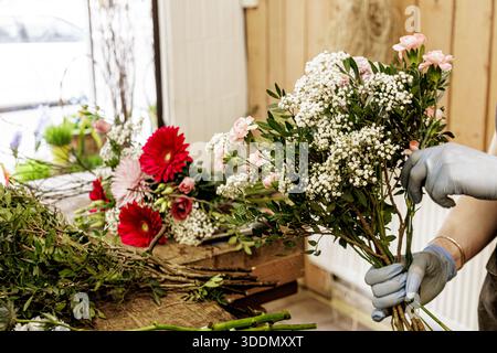 Fiorista che organizza un mazzo di fiori rosa e bianchi in un negozio di fiori, festa della mamma Foto Stock