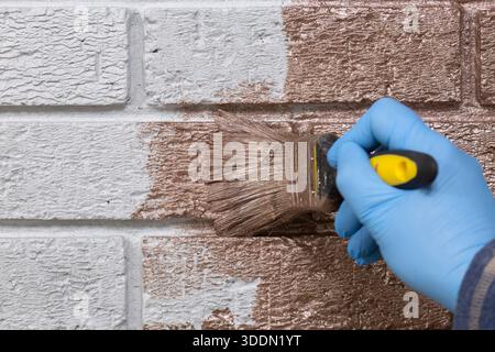 Persona che dipinge su una parete di mattoni grigi con vernice metallizzata oro rosa utilizzando un pennello. Fai da te il concetto di miglioramento della casa. Foto Stock