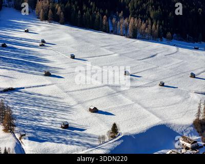 Vista aerea dell'abbraccio invernale, dove i campi innevati incontrano il fascino rustico dei fienili in legno, un paesaggio sereno sotto un cielo limpido, Sesto, trenta Foto Stock
