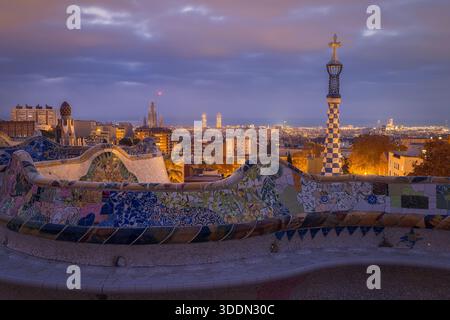 La luce soffusa del mattino bagna il Parco Guell, rivelando mosaici colorati e ampie vedute dello skyline di Barcellona, creando un'atmosfera tranquilla e incantevole Foto Stock