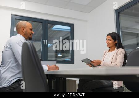 Riunione d'affari in un ufficio di una società industriale, un candidato afroamericano maschio in un colloquio di assunzione con una giovane manager indiana. Foto Stock