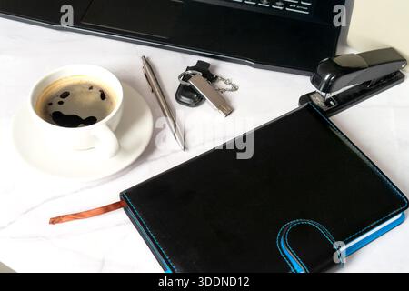 Tazza da caffè accanto a Planner e laptop, chiavi, penna, cucitrice su una scrivania pulita area di lavoro mattutina minimalista per consulenti freelance che preparano il programma e il Co Foto Stock