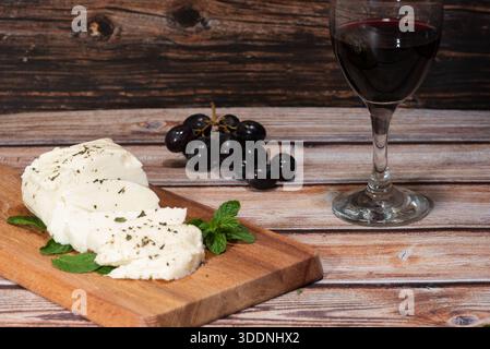 Piatto tradizionale di formaggio halloumi, uva e vino rosso su un tavolo di legno. L'halloumi fa parte della dieta mediterranea Foto Stock