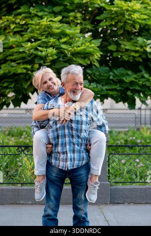 Felice coppia senior che si diverte e si diverte con un giro all'aperto sul piggyback Foto Stock