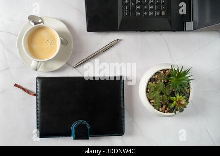 Tazza di caffè accanto al taccuino in pelle, succulento in pentola, penna argento, telefono per ufficio su superficie in lino bianco. Calmo e minimalista Morning Flatlay per Entrepre Foto Stock