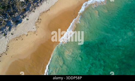 Una vista aerea mostra il sereno incontro tra spiaggia sabbiosa e onde turchesi dell'oceano, evidenziando la tranquilla bellezza della natura. Foto Stock