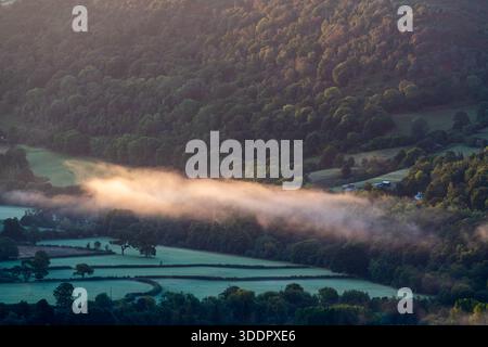 La nebbia dell'alba attraversa una valle boscosa illuminata da una luce calda Foto Stock