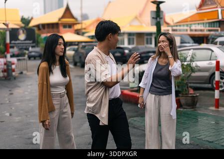 Gruppo di amici asiatici che hanno una conversazione seria all'aperto, discutendo problemi o problemi di relazione Foto Stock