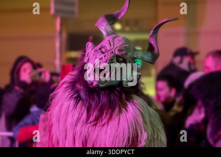 Un krampus con corna è illuminato con luce rosa durante la processione del festival Foto Stock
