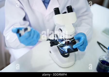 Uno scienziato professionista aziona meticolosamente un microscopio e una pipetta potenti in un ambiente di laboratorio incontaminato che conduce attività scientifiche critiche Foto Stock