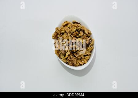 Cereali granola croccanti serviti in una ciotola bianca su uno sfondo pulito, un concetto di colazione sana con avena, cereali e texture naturale Foto Stock