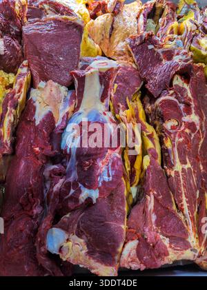 Grossi tagli di carne cruda con grasso e ossa visibili sistemati in macelleria. L'abbondante esposizione evoca un'atmosfera rustica e primitiva, mostrando carne di qualità. Foto Stock