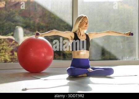 Donna di mezza età sottile che si allena a casa con manubri e palla di stabilità Foto Stock