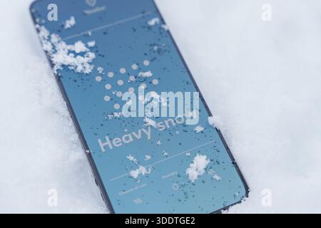 Smartphone sdraiato all'aperto in presenza di neve intensa con schermata dell'app meteo che mostra le previsioni della neve Foto Stock