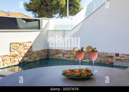 Elegante allestimento a bordo piscina con due cocktail, piatto di pesce e rilassante atmosfera estiva Foto Stock