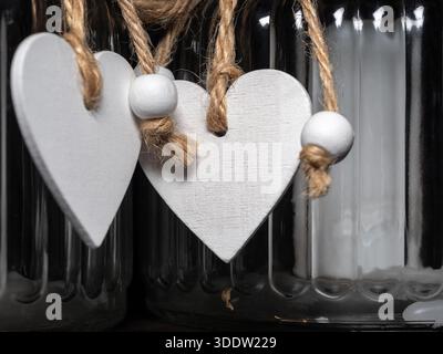 Decorazioni rustiche con forma a cuore in legno bianco sospese da corde di spago all'interno di una bottiglia di vetro, per creare un'affascinante e romantica vignetta perfetta per Foto Stock