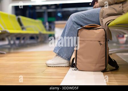 Primo piano dello zaino accanto a una donna seduta nel terminal dell'aeroporto Foto Stock