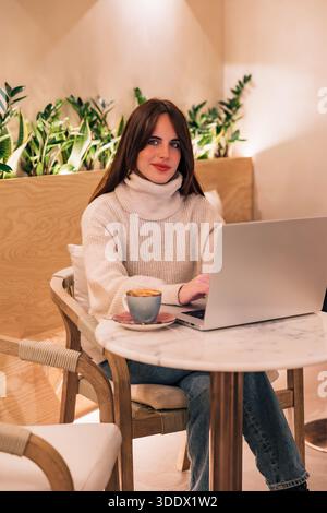 Giovane donna che lavora a distanza in un accogliente bar Foto Stock