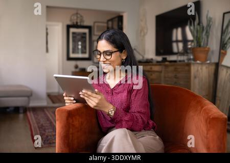 Felice giovane donna indiana guardare o leggere contenuti su tablet Foto Stock
