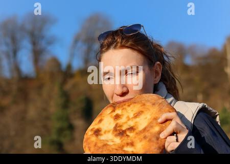 Ritratto di una donna beatamente che mangia la focaccia nell'ambiente della foresta autunnale, il cielo blu che esalta l'atmosfera serena. Foto Stock