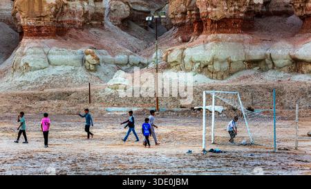 Ragazzi che giocano a calcio sotto al Qarah Mountain, al Ahsa Oasis, Hofuf, Arabia Saudita Foto Stock