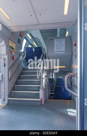 Scatto verticale grandangolare che mostra la cabina pulita e futuristica di un treno pendolare con scale che portano al ponte superiore e file di sedili Foto Stock