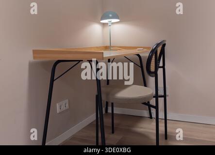 Immagine orizzontale ad angolo ampio di un'elegante scrivania in legno con gambe in metallo nero, una sedia in rattan e una lampada da scrivania verde illuminata in un angolo accogliente Foto Stock