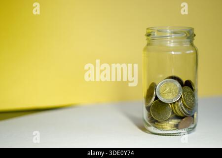 Monete in euro in vaso di vetro su fondo giallo Foto Stock