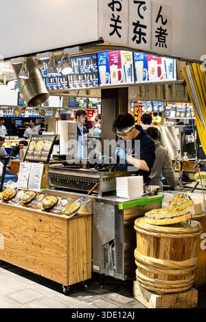 Uomo che cucina okonomiyaki in uno stand di cibo di strada nel mercato di Kuromon, Osaka, Giappone Foto Stock