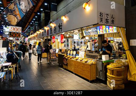 Uomo che cucina okonomiyaki in uno stand di cibo di strada nel mercato di Kuromon, Osaka, Giappone Foto Stock