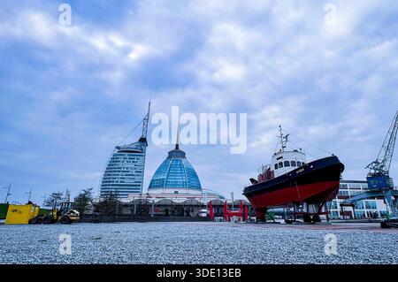 Bremerhaven, Deutschland, Europa. Außenansicht des Museumshafens mit dem historischen Schiff Seute Deern aufgebockt an Land, umgeben von Hafeninfrastruktur. Im Hintergrund moderne Wahrzeichen wie das KlimaHaus Bremerhaven und das Atlantic Hotel Sail City, Hafenkräne sowie Hochhausbebauung. Weitwinkelaufnahme aus niedriger Perspektive, offener Platz mit Pflaster und Schotter, bewölkter Himmel. Stadtentwicklung, Tourismus, Maritime Geschichte, Architektur, Gesellschaft, Hafen, Symbolfoto. *** Bremerhaven, Germania, Europa Vista esterna del porto del museo con la storica nave Seute Deern jacke Foto Stock