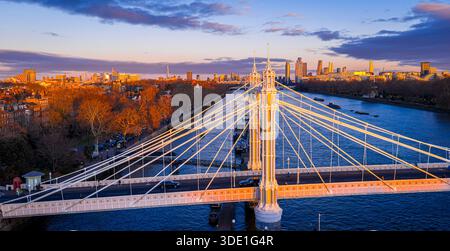Vista panoramica dell'Albert Bridge sul fiume Tamigi all'ora d'oro, che collega Chelsea e Battersea mentre lo skyline di Londra si illumina; per i viaggi, i trasporti, Re Foto Stock