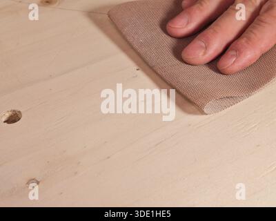 Levigatura manuale del legno con primo piano in rete abrasiva; primo piano di un falegname o di un appassionato di fai da te utilizzando una moderna carta abrasiva a rete per levigare e pre-levigare Foto Stock