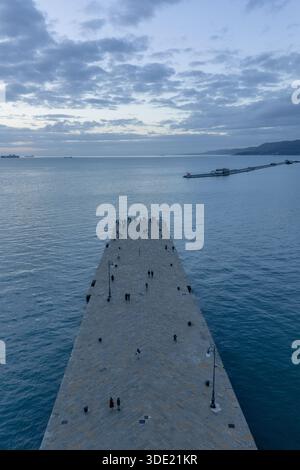 Veduta aerea di un lungo molo che si estende nelle acque calme e blu sotto un vasto cielo nuvoloso, la LHD Trieste, Trieste, Italia. Foto Stock