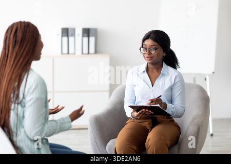 Amichevole psicologa afroamericana che ha una sessione con cliente femminile in ufficio. Consulenza psicoterapeutica Foto Stock