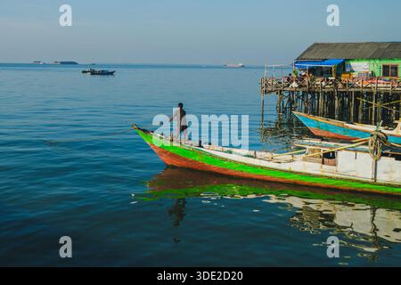 Balikpapan, Indonesia - 8 novembre 2025. Un pescatore a bordo di una barca tradizionale dai colori vivaci sta attivamente tirando la sua linea di ancoraggio per riposizionarla Foto Stock