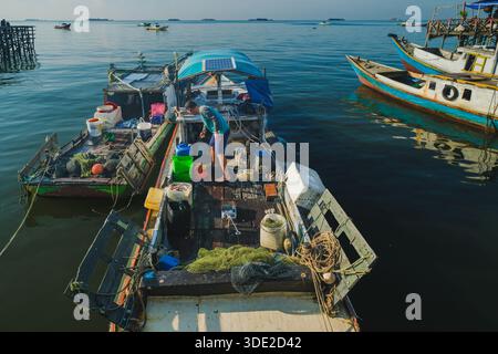 Balikpapan, Indonesia - 8 novembre 2025. Una vista rialzata cattura un pescatore che lavora tra container e attrezzatura da pesca sul disordinato ponte di legno di Foto Stock