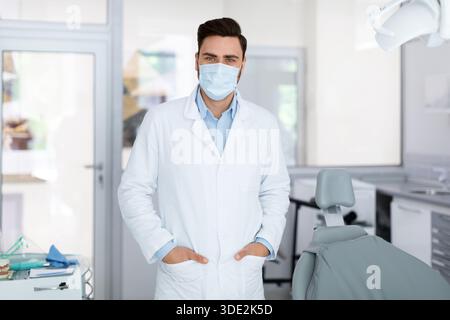 Giovane medico in maschera in piedi presso la clinica dentale Foto Stock