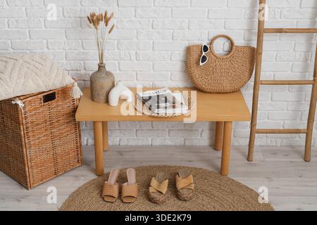 Panca in legno con borsa, riviste e vaso vicino a pareti in mattoni bianchi all'interno della sala, primo piano Foto Stock