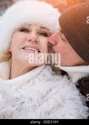Amanti che si scambiano affetto in climi freddi, coppia che mostra calore e amore durante il freddo giorno invernale, uomo e donna che condividono un tenero bacio sulla guancia Foto Stock