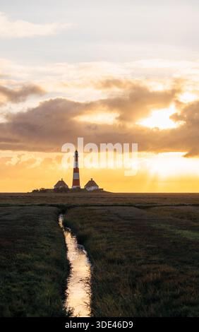 Faro di Westerheversand nella palude costiera al tramonto dorato del cielo Foto Stock