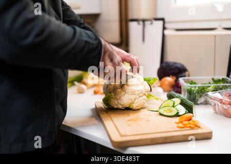 Primo piano di uno chef professionista che prepara gli ingredienti per i pasti vegetariani nella cucina del ristorante. Sta tagliando il cavolfiore. Foto Stock