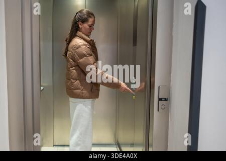 Donna che apre la porta dell'ascensore nel corridoio dell'edificio di appartamenti. Movimento quotidiano all'interno dello spazio residenziale. Foto Stock