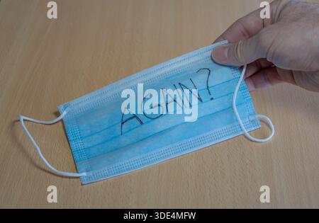 mano che tiene una maschera con la domanda di nuovo? scritto sopra Foto Stock