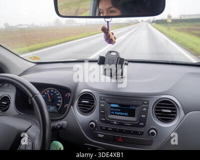 Riprese POV dall'interno di un'auto, guardando il cruscotto e la strada bagnata davanti a una giornata nuvolosa Foto Stock